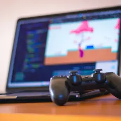 Gamepad do PS4 leży przed laptopem z kodem i grą na ekranie. Dowiedz się, jak podłączyć PS4 do laptopa, by grać gdziekolwiek.