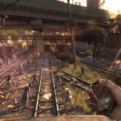 Gracz z granatem w ręku, otoczony przez hordę zombie na torach kolejowych. To scena z gry Dying Light, gdzie wymagania sprzętowe są kluczowe dla płynności rozgrywki.