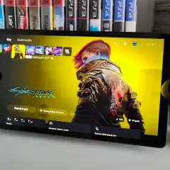 Ps5 Portal z grą Cyberpunk 2077, obok kontroler DualSense. W tle gry na PS4 i PS3.
