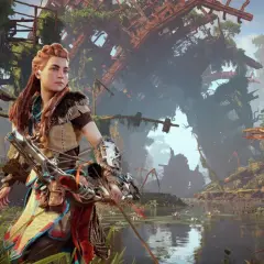 Aloy w Horizon Zero Dawn Remastered, z łukiem w ręku, stoi nad wodą wśród bujnej roślinności i zrujnowanych budowli.