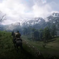 Jazda konno przez górzyste tereny w Red Dead Redemption 2 PC. Śnieżne szczyty gór i zielone lasy tworzą zapierający dech w piersiach krajobraz.