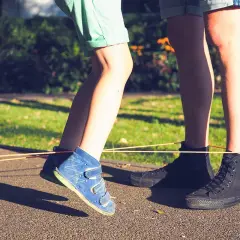 Dzieci skaczą przez gumę, odtwarzając ulubione gry z dzieciństwa. Słońce oświetla ich nogi w kolorowych butach.