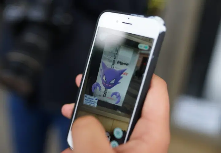 Ręka trzyma smartfon, na ekranie którego widnieje fioletowy Haunter, jeden z typów pokemonów.