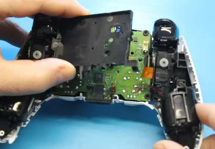 Rozkręcony pad PS5, widoczna płyta główna i elementy mechaniczne. Trwa naprawa pada PS5.
