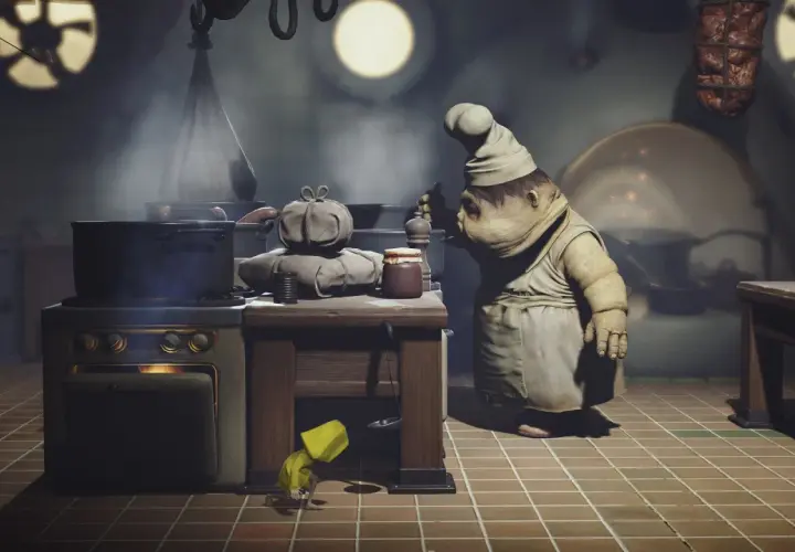 Mały kucharz z Little Nightmares gotuje w kuchni. Pod stołem ukrywa się dziewczynka w żółtym płaszczu.