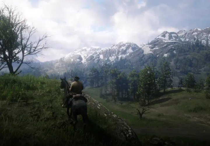Jazda konno przez górzyste tereny w Red Dead Redemption 2 PC. Śnieżne szczyty gór i zielone lasy tworzą zapierający dech w piersiach krajobraz.