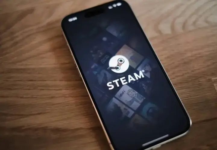 Telefon z aplikacją Steam, gdzie widać logo i okładki gier. W tle delikatna **steam cloud** unosząca się nad ekranem.
