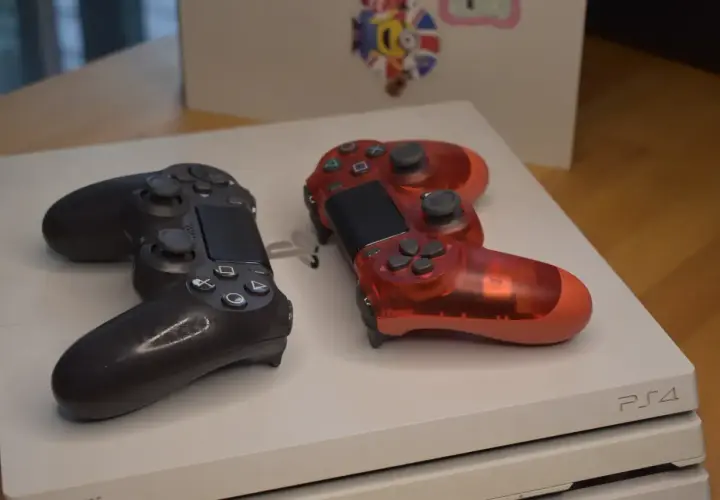 Dwa kontrolery, czarny i przezroczysty czerwony, leżą na białej konsoli PS4. Pamiętasz, kiedy wyszło PS4?