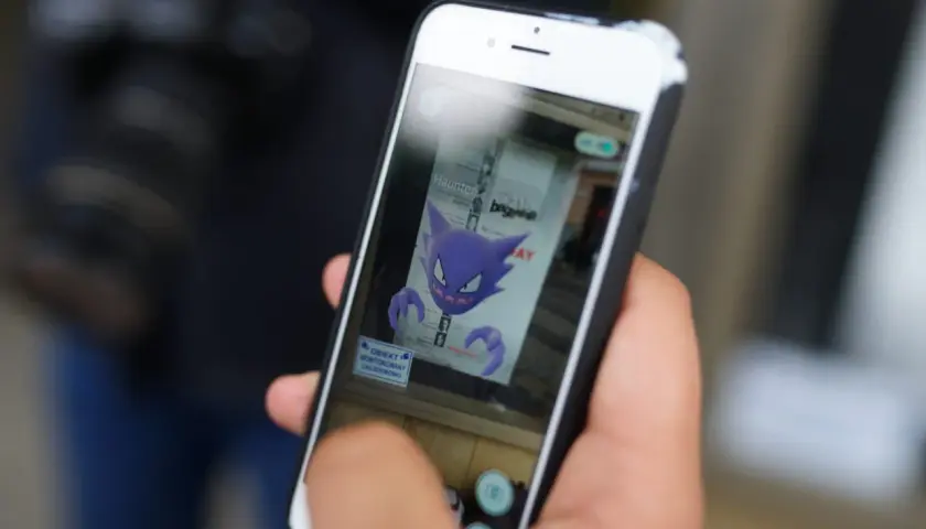 Ręka trzyma smartfon, na ekranie którego widnieje fioletowy Haunter, jeden z typów pokemonów.