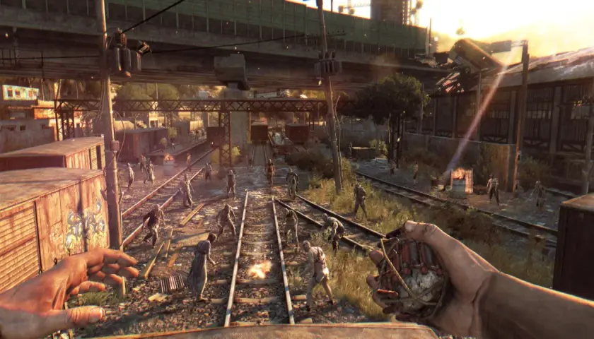 Gracz z granatem w ręku, otoczony przez hordę zombie na torach kolejowych. To scena z gry Dying Light, gdzie wymagania sprzętowe są kluczowe dla płynności rozgrywki.