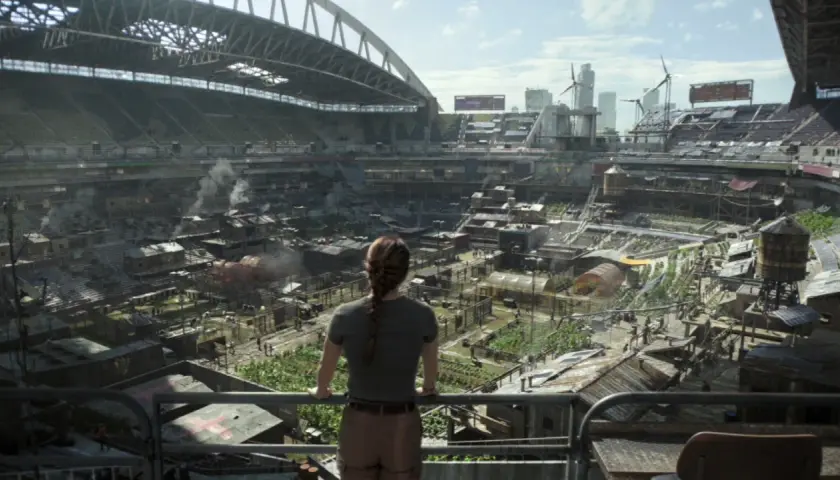 Widok na postapokaliptyczne miasto wewnątrz stadionu, gdzie ludzie żyją w prowizorycznych domach. Może to być scena z The Last of Us sezon 3.