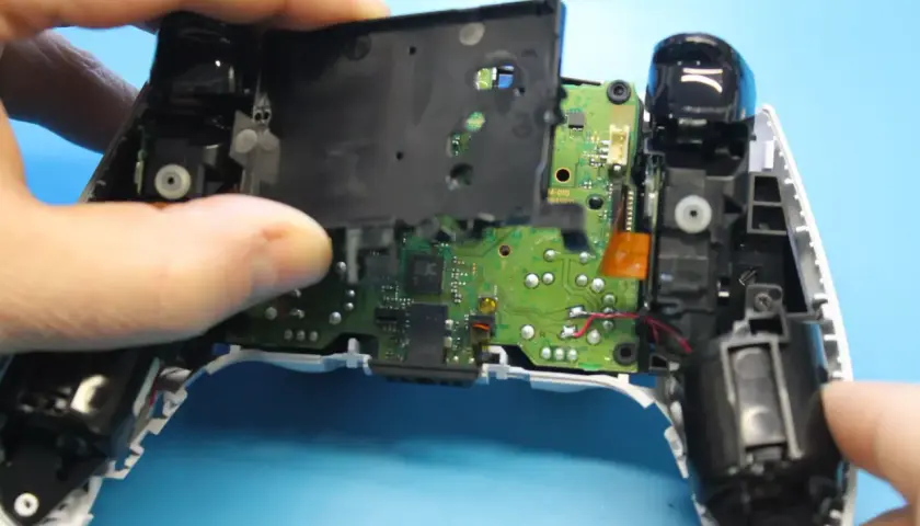 Rozkręcony pad PS5, widoczna płyta główna i elementy mechaniczne. Trwa naprawa pada PS5.