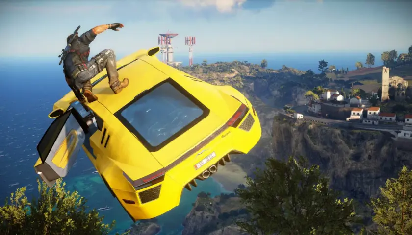 Rico z Just Cause 5 skacze z żółtego supersamochodu nad klifem, w tle widać śródziemnomorską wioskę i morze.