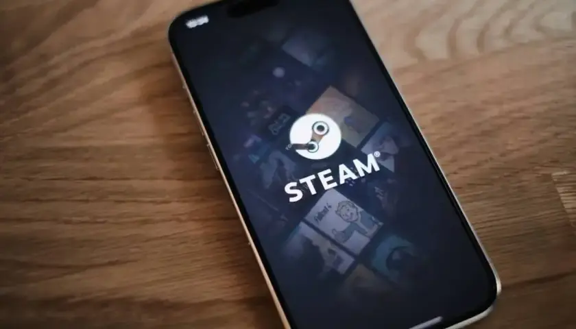Telefon z aplikacją Steam, gdzie widać logo i okładki gier. W tle delikatna **steam cloud** unosząca się nad ekranem.