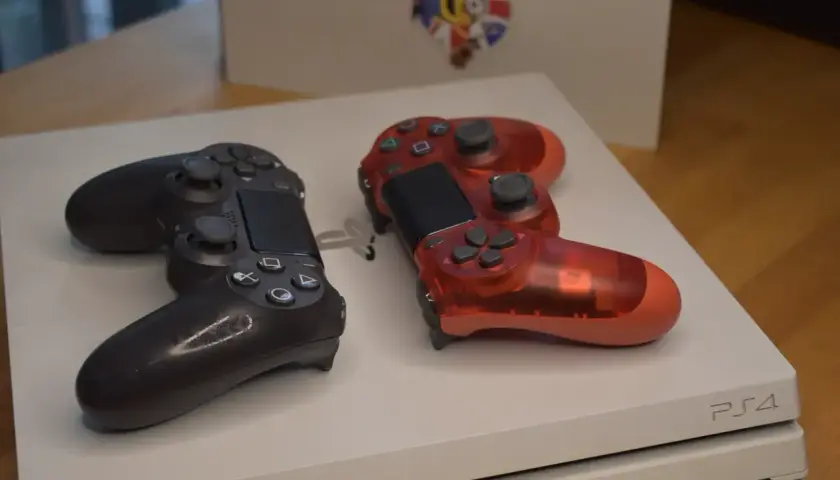 Dwa kontrolery, czarny i przezroczysty czerwony, leżą na białej konsoli PS4. Pamiętasz, kiedy wyszło PS4?