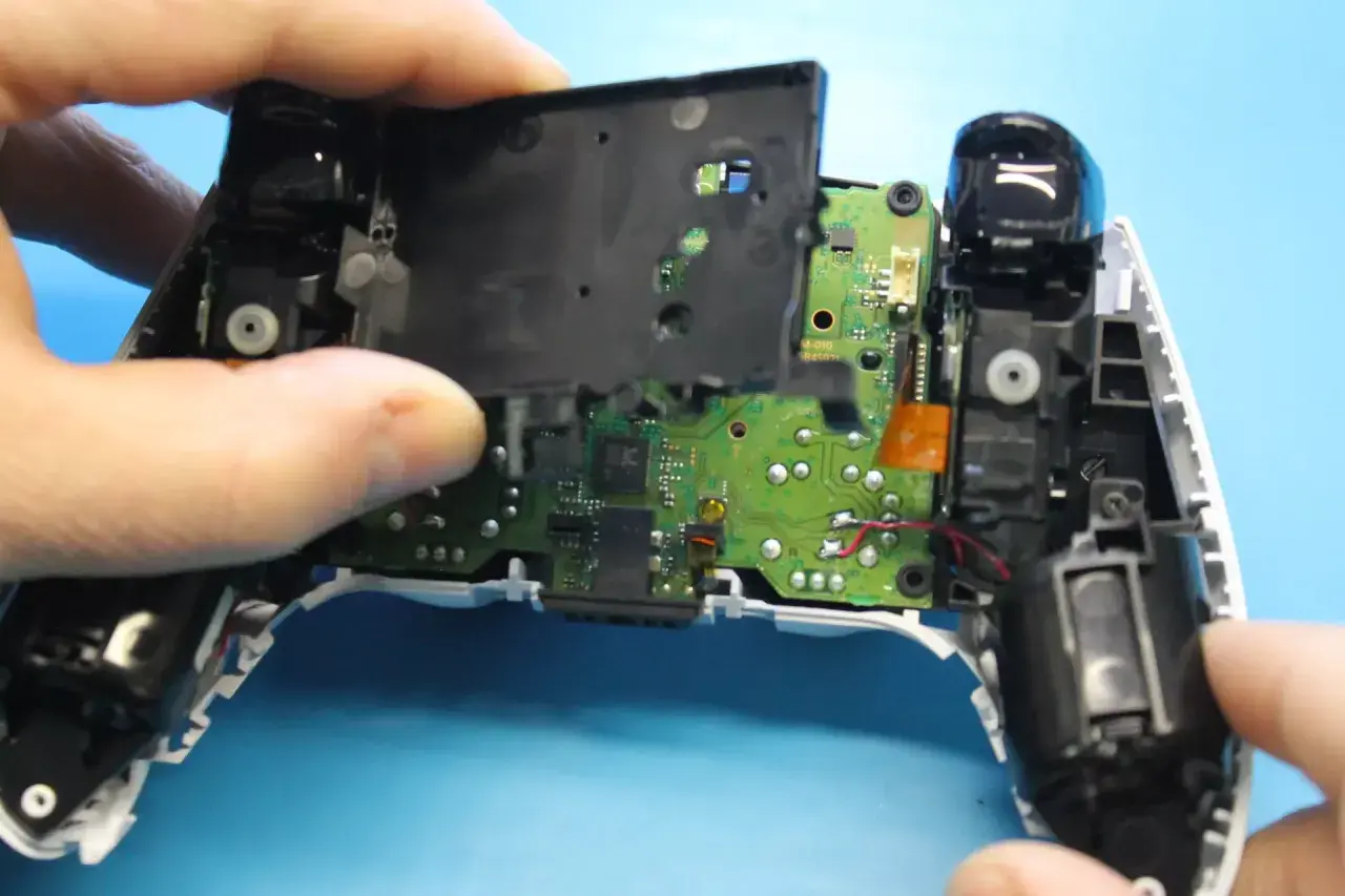 Rozkręcony pad PS5, widoczna płyta główna i elementy mechaniczne. Trwa naprawa pada PS5.