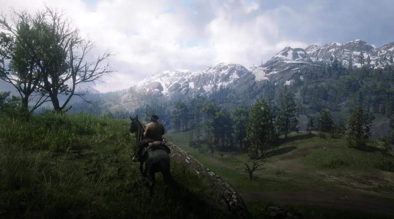 Jazda konno przez górzyste tereny w Red Dead Redemption 2 PC. Śnieżne szczyty gór i zielone lasy tworzą zapierający dech w piersiach krajobraz.