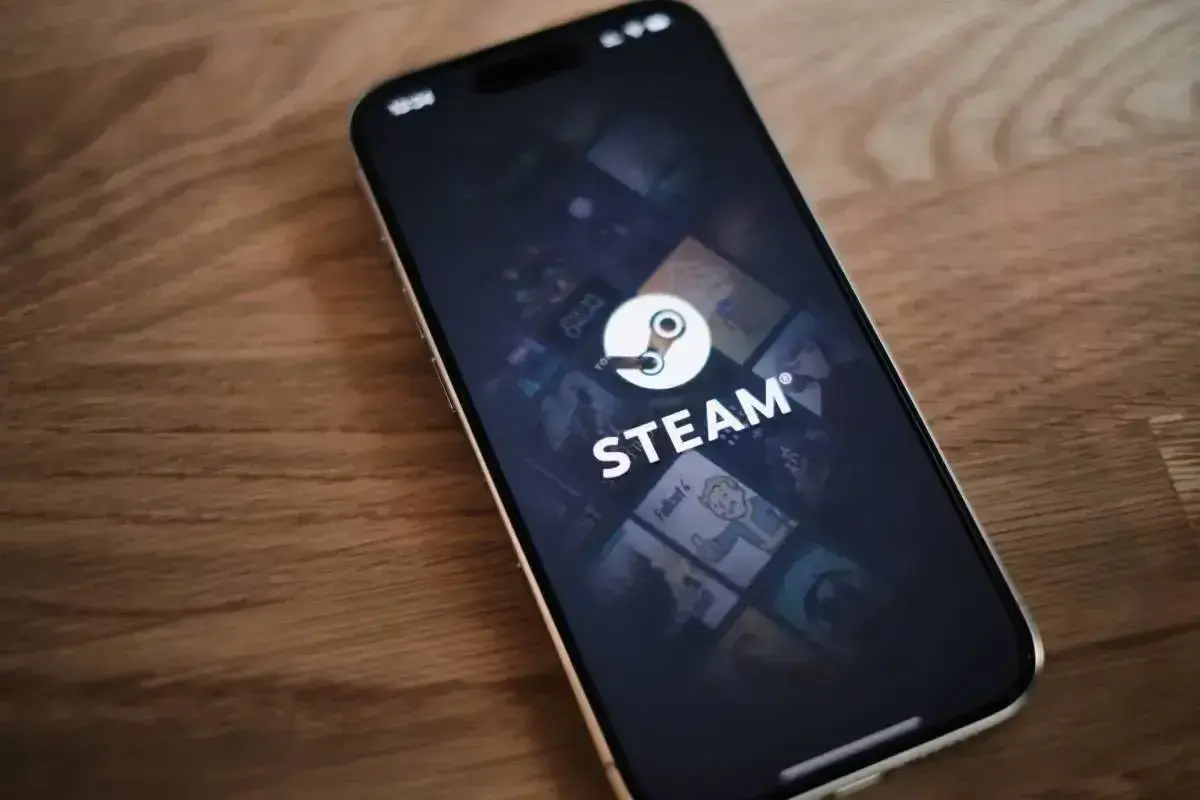 Telefon z aplikacją Steam, gdzie widać logo i okładki gier. W tle delikatna **steam cloud** unosząca się nad ekranem.