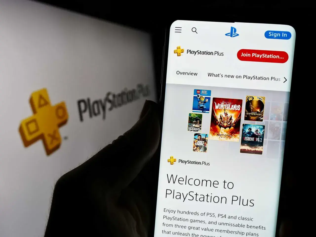 Gry co miesiąc PS Plus na ekranie telefonu, obok logo PlayStation Plus.