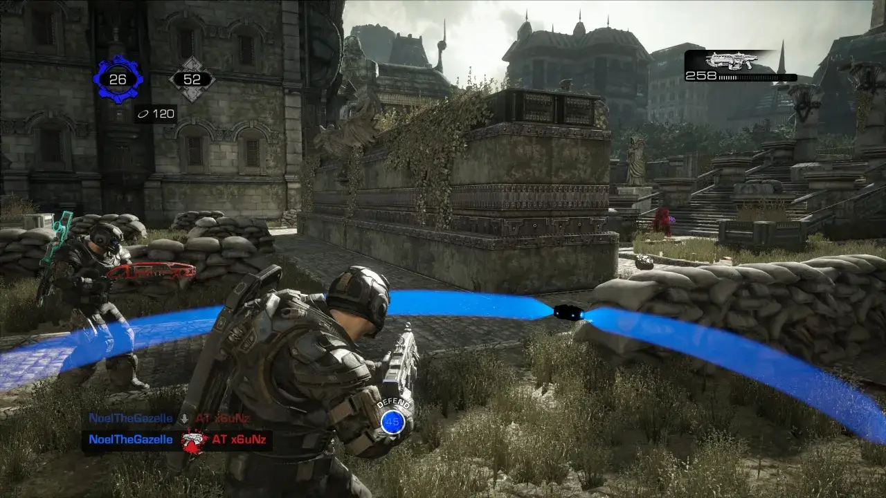 Gracze w Gears of War na PS5 w akcji, ukryci za workami z piaskiem, celują z broni. W tle ruiny miasta.